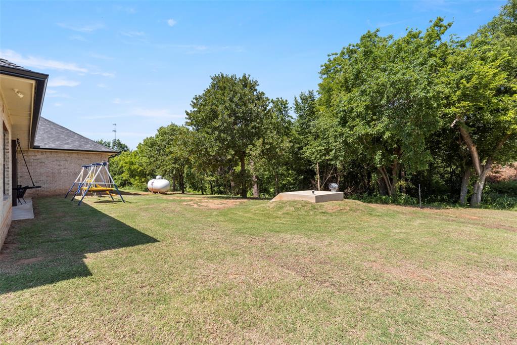 Tessa Hood Realtor – Spacious backyard with in-ground storm shelter and wooded pond-access area at 1074 Fawn Meadow Dr, Blanchard Oklahoma